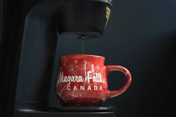 Fresh coffee pouring from machine into a red cup. Espresso dripping from coffee machine. Flow of fresh ground coffee. Niagara Falls Canada text on the cup