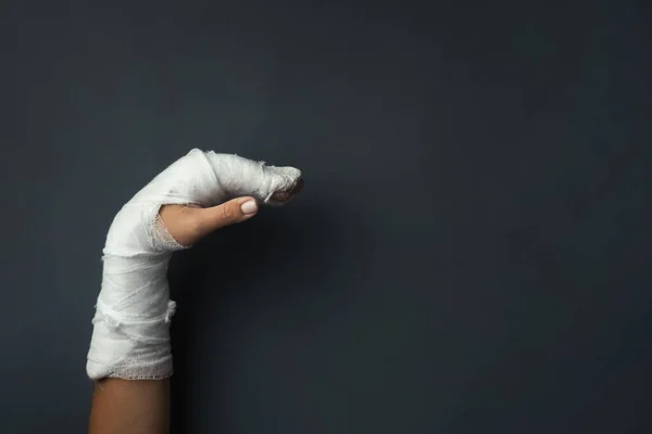 Woman hand with a cast  on the dark grey background with copy space for text. Girl has a broken arm