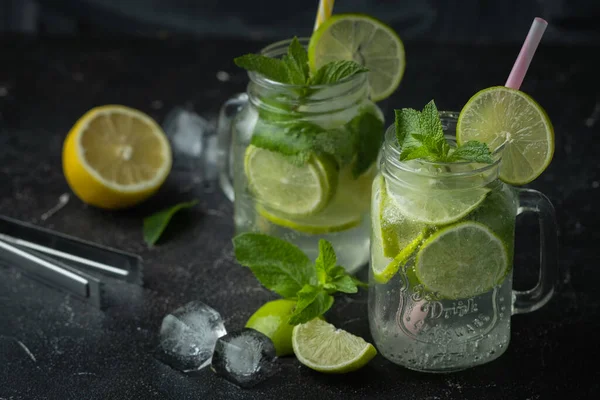 Refreshment mojito cocktail with mint and lime in a glass mug on a black background. Cold summer drink with ice