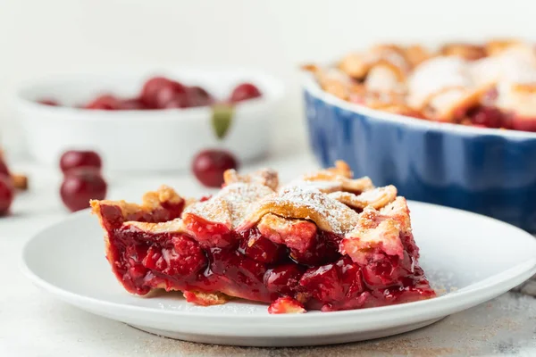 Piece of delicious homemade cherry pie with Flaky Crust sprinkled with powdered sugar on the white marble background. American traditional cherry tart.