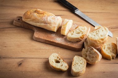 Whole grain bread close-up on the wooden cutting board. Knife with serrated blade. Fresh bread on the wooden kitchen table. Flat lay with traditional pastries in bakery