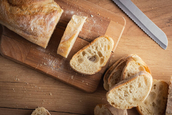 Whole grain bread close-up on the wooden cutting board. Knife with serrated blade. Fresh bread on the wooden kitchen table. Flat lay with traditional pastries in bakery