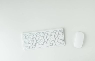 White GWERTY keyboard and mouse on the white table surface. Working place concept. Flat lay of office desk. Copy space for a text