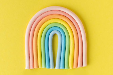 Cartoon edible rainbow made of confectionery mastic on the yellow background. Multicolored cake topper. Decoration for a cake