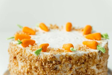 Delicious carrot cake decorated with mastic sweet carrots. Homemade carrot cake with yellow crumbs in the white plate on the white background