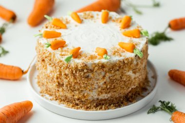 Delicious carrot cake decorated with mastic sweet carrots. Homemade carrot cake with yellow crumbs in the white plate on the white background