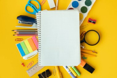 Blank notepad for free text next to the school supplies on the yellow background. Back to school concept on September day. Flat lay. Free space.