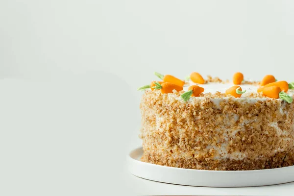 Delicious carrot cake decorated with mastic sweet carrots. Homemade carrot cake with yellow crumbs in the white plate on the white background