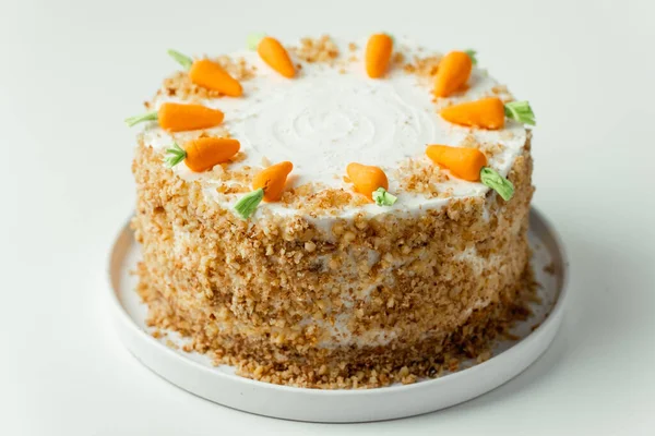 Delicious carrot cake decorated with mastic sweet carrots. Homemade carrot cake with yellow crumbs in the white plate on the white background