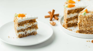 Delicious carrot cake decorated with mastic sweet carrots next to white cup of tea. Slice of homemade carrot cake with yellow crumbs in the white plate on the white background