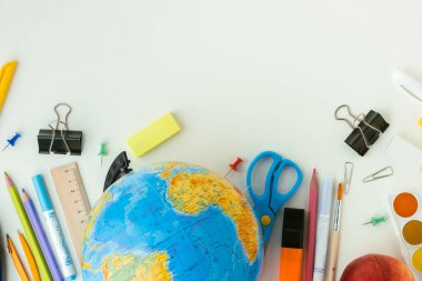 School supplies next to the globe and red apple on white background. Back to school concept on September day. Flat lay. Free space