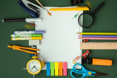 Blank notepad for free text next to the school supplies on the green background. Back to school concept on September day. Flat lay. Free space.
