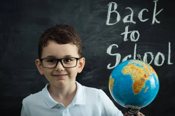 Cute Caucasian Schoolboy Wearing Glasses Holding Globe Black School Board — ストック写真