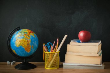 School supplies next to the globe and stack of books on the blackboard background. Back to school concept on September day