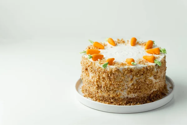 Delicious carrot cake decorated with mastic sweet carrots. Homemade carrot cake with yellow crumbs in the white plate on the white background