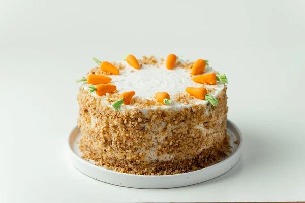 Delicious carrot cake decorated with mastic sweet carrots. Homemade carrot cake with yellow crumbs in the white plate on the white background