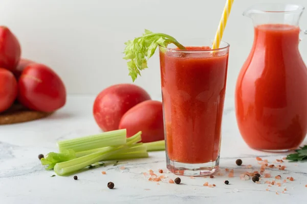 Fresh tomato juice in a glass with a straw on the white background. Red tomato juice cocktail with tomatoes and celery