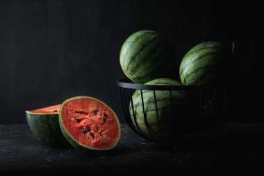 Many green striped watermelons and one red juicy cut watermelon on the black background. Summertime background