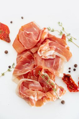 Slices of dried spanish ham with Italian sun-dried tomatoes. Jamon Serrano on the white background. Flat lay