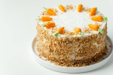 Delicious carrot cake decorated with mastic sweet carrots. Homemade carrot cake with yellow crumbs in the white plate on the white background