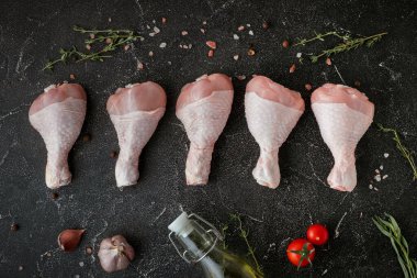 Çiğ tavuk budu, baharat ve bitkilerle. Siyah arka planda tavuk budu üst görünümü.