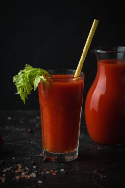 Fresh tomato juice in a glass with a straw on the black background. Red tomato juice cocktail with tomatoes and celery