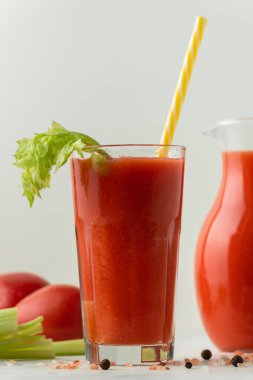 Fresh tomato juice in a glass with a straw on the white background. Red tomato juice cocktail with tomatoes and celery