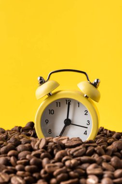 Sarı arkaplandaki kahve çekirdekleri yığınının içindeki sarı alarm saati. Sabah konseptinde erken kalkmak. Boşluğu kopyala
