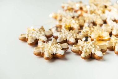 Kartanesi şeklinde zencefilli kurabiye ve altın renkli krema. Beyaz arka planda çelenk ışıkları olan Noel kurabiyeleri. Mutlu yıllar..