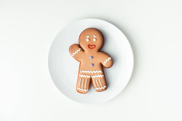 Gingerbread man with festive icing on white plate. Christmas cookie on white background. Happy New Year. Flat lay