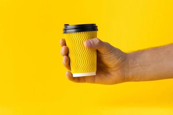 Man hand holding  yellow paper cup of coffee on a yellow background. Disposable paper cup. Save the planet concept. Getting up early in the morning
