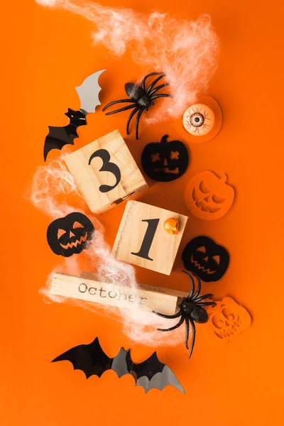 Flat lay of scary bats, spiders with cobweb on the orange background. orange and black pumpkins.  Wooden calendar of blocks with the date of October 31 on the Halloween background