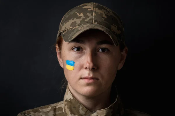 stock image Portrait of beautiful girl with yellow and blue ukrainian flag on her cheek wearing military uniform. Ukrainian women in the army. Black background. Stand with Ukraine