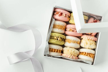 Beyaz arka planda çok renkli badem kurabiyeleriyle dolu bir hediye kutusu. Fransız tatlısı