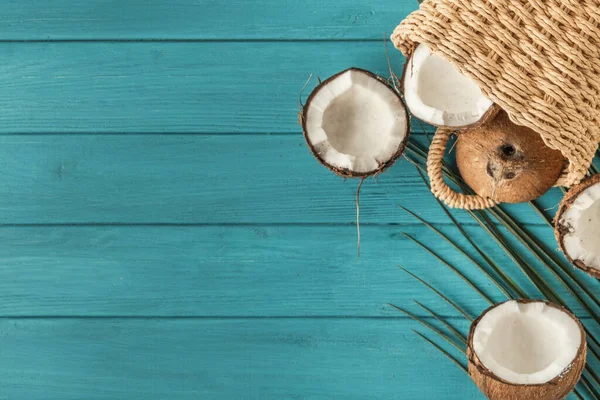 Coconut pieces with green palm leaves. Tropical fruit on the wooden turquoise background. Flat lay