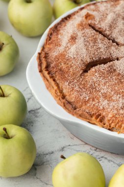 Beyaz mermer arka planda ev yapımı elmalı turta ve yeşil elmalarla çevrili tarçın aromalı gevrek kabuklu şeker..
