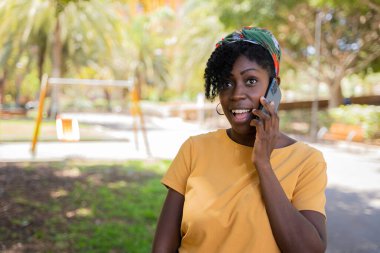 Siyah kadın sokakta cep telefonuyla konuşurken el kol hareketi yapıyor.