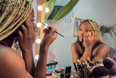 Afro genç kadın makyaj yapıyor.