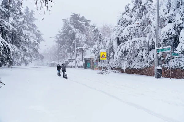 Människor som bär vagnar på en stadsgata täckt av snö under kraftiga snöstormar i Madrid — Stockfoto