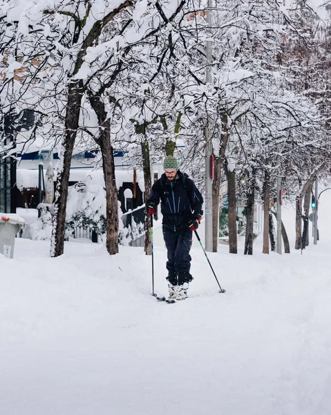Man skidåkning på en stadsgata täckt av snö under tungt snöfall med fallna träd — Stockfoto