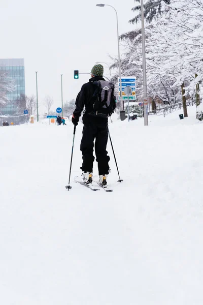 Man skiing on a city street covered in snow during heavy snowfall with fallen trees — Stock Photo, Image