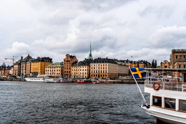 Barca tour con bandiera svedese che naviga contro il lungomare di Stoccolma — Foto Stock