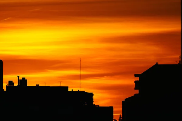 Dramatisch bewölkter Himmel bei Sonnenuntergang im Stadtgebiet. Silhouettenbauten am orangen und gelben Himmel — Stockfoto