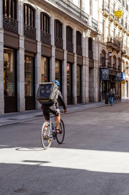 Madrid, Spain - October 11, 2020: Man courier on bicycle delivering food in town street with a hot food delivery from restaurants to home, express food delivery and shopping online concept.
