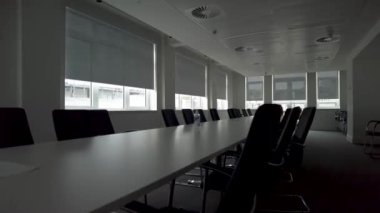 Beyaz ve siyah ofis konferans salonunun beyaz dikdörtgen masa, deri sandalyeler ve pencereler, yan görüş. Ofis minimalist mobilyalar, klima ve yangın alarmı, beyaz zemin.