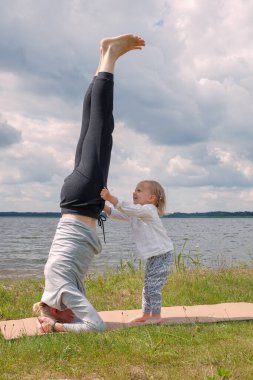 Baba çocukla oynuyor ve göl kenarında yoga egzersizi yapıyor.