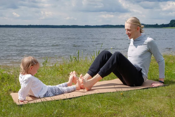 Padre jugar con el niño y hacer ejercicio de yoga al aire libre cerca del lago — Foto de Stock