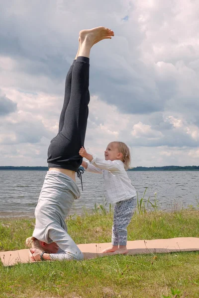 Ojciec bawi się z dzieckiem i ćwiczy jogę na świeżym powietrzu w pobliżu jeziora — Zdjęcie stockowe