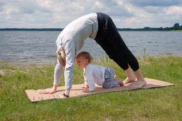 Far leker med barn och yogautövande utomhus nära sjön — Stockfoto