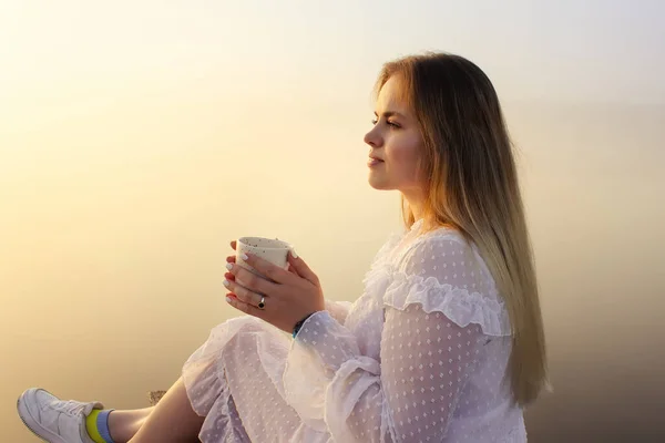 Woman drink coffee and enjoy the beautiful foggy lake and nature at sunrise